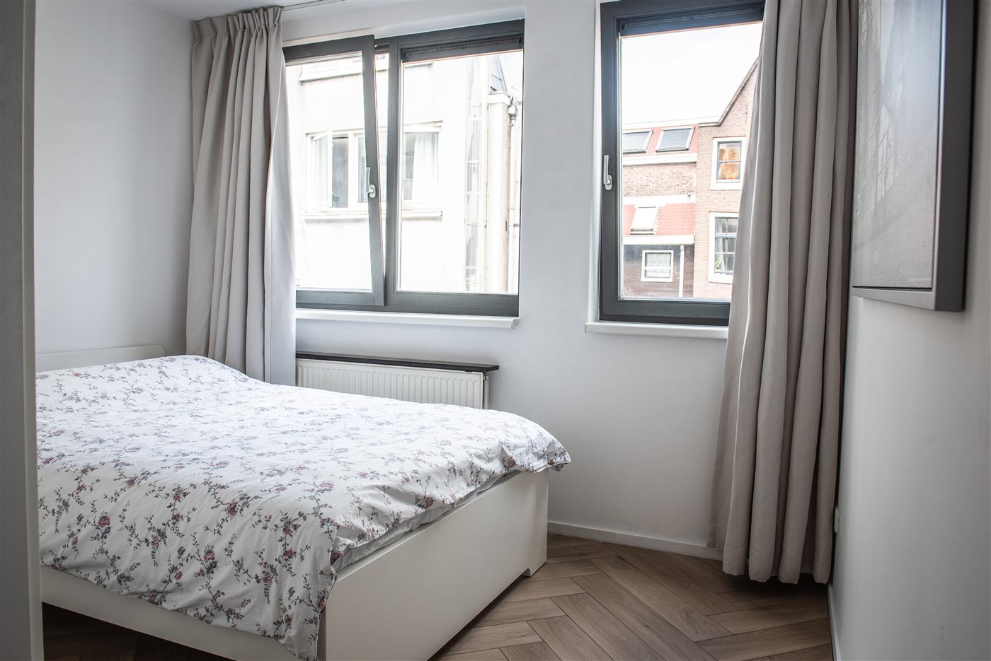 Bedroom with a double bed under two windows, curtains drawn back.