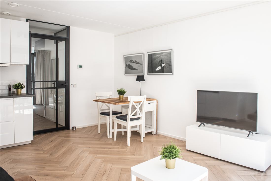 Dining table for two beside a steel-framed partition, with a television on a low white cabinet.