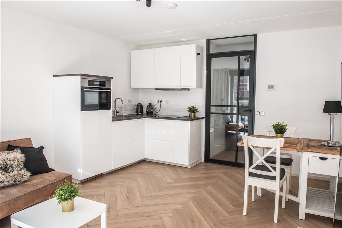 White kitchen with oven, induction hob and a steel-framed glass door through to the dining area.