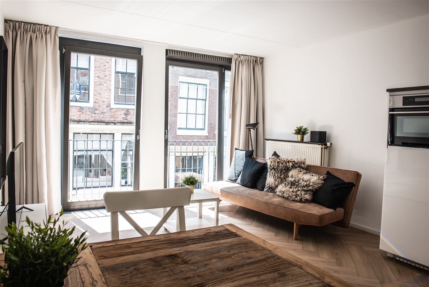 Living room with a low wooden sofa, two tall windows onto the canal and a herringbone oak floor.